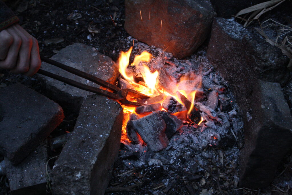 a hand gripping a blacksmith tongs, holding hot metal in a forge fire.